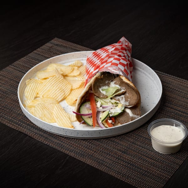 Gyro wrap with meat, vegetables, and sauce, served with potato chips and a side of dressing.