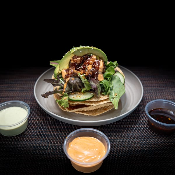 Tuna poke tostada with avocado, greens, and cucumber, served with three dipping sauces.