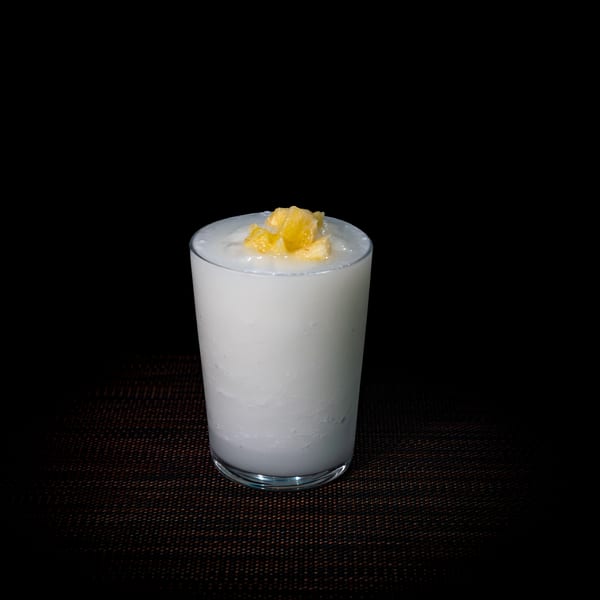 A white, creamy drink in a clear glass, topped with small pieces of yellow fruit.