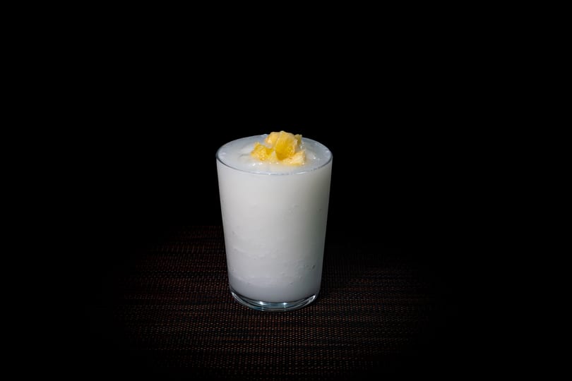 A white, creamy drink in a clear glass, topped with small pieces of yellow fruit.