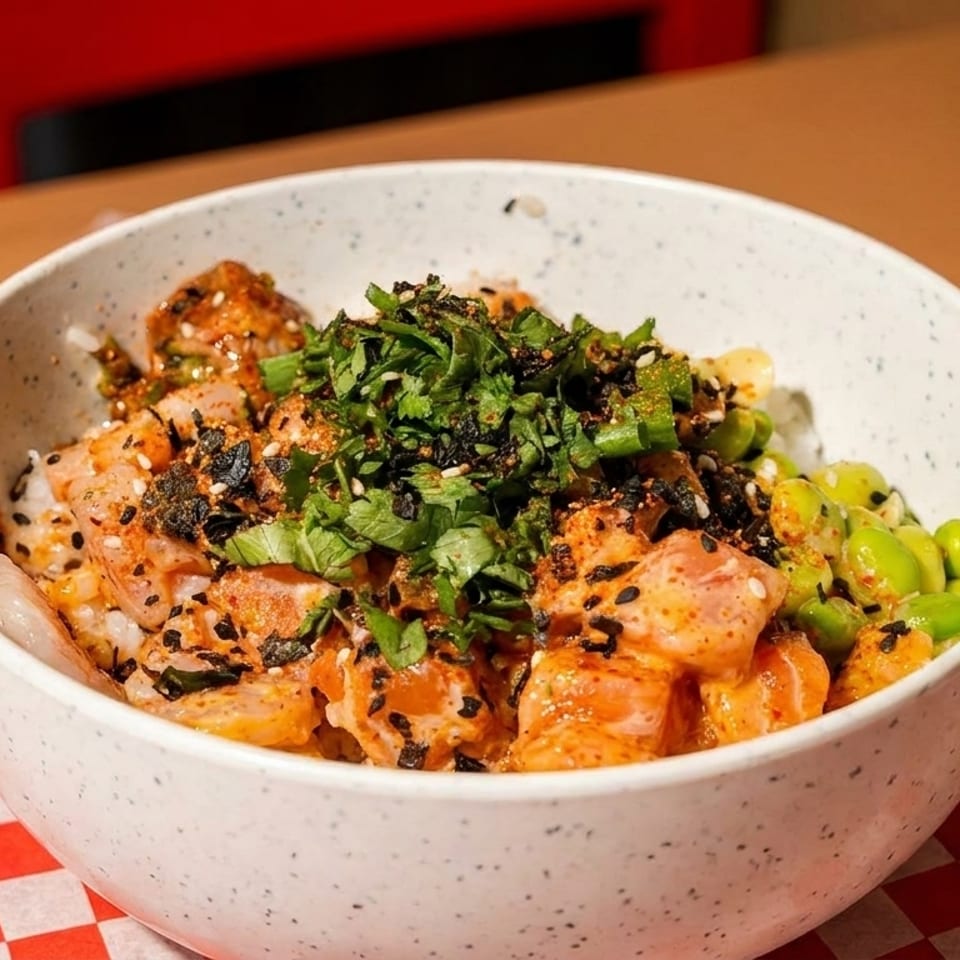 A colorful poke bowl with salmon, edamame, and herbs on a red and white checkered paper.