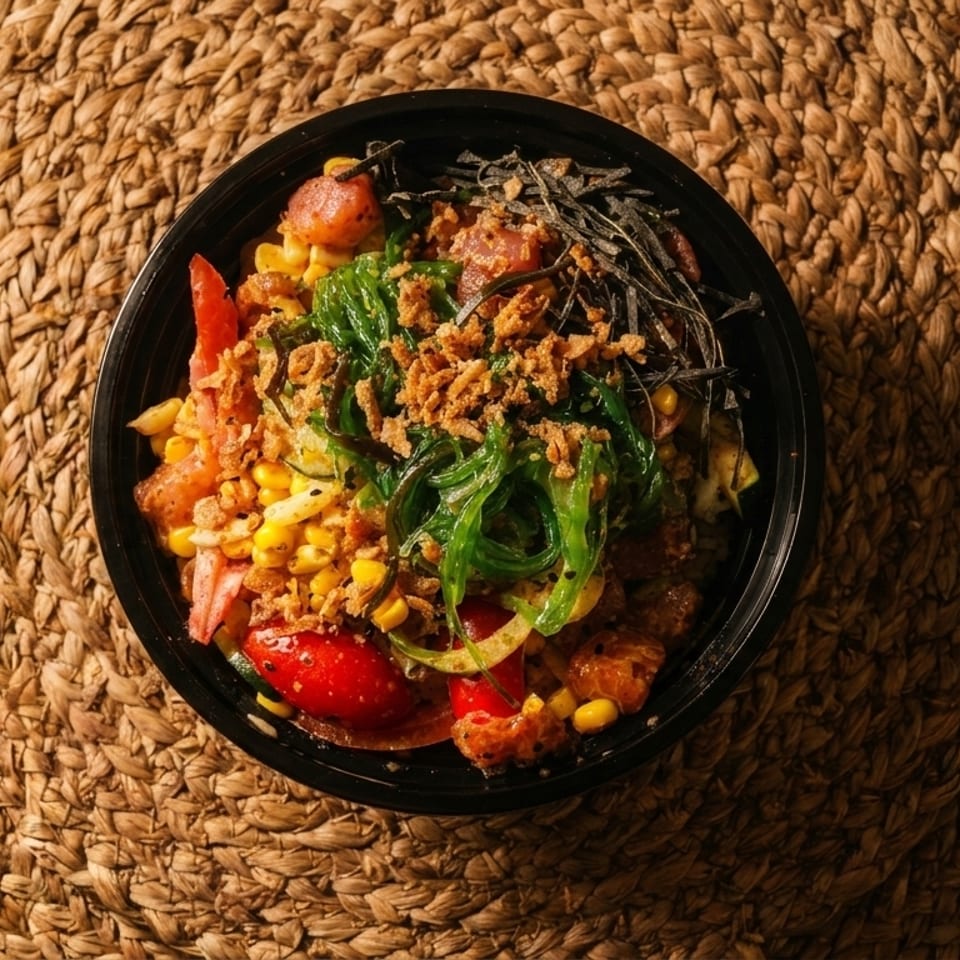 Overhead view of a colorful poke bowl with tuna, corn, seaweed, and crispy onions on a woven mat.